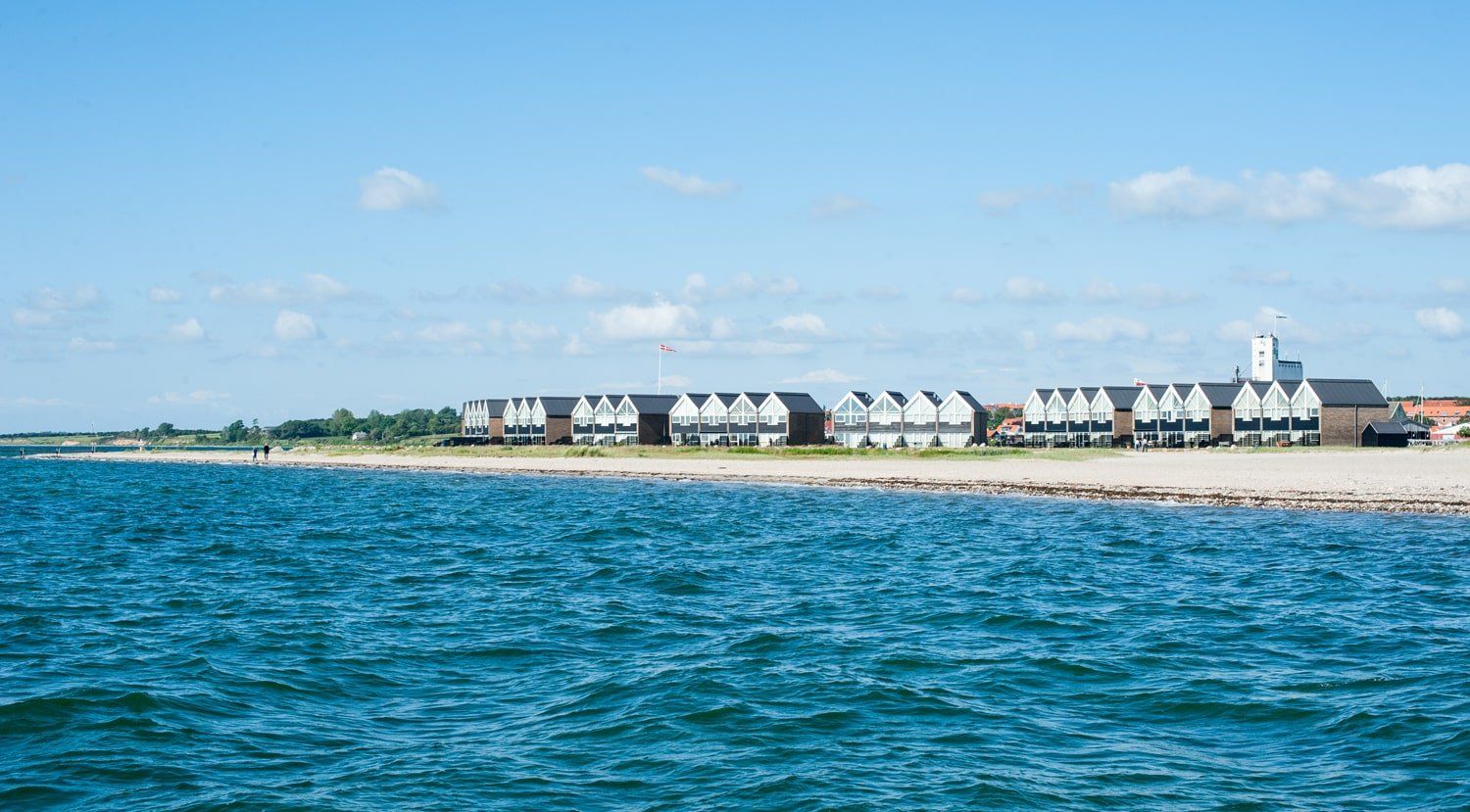 En række huse på en strand ved siden af ​​en vandmasse.