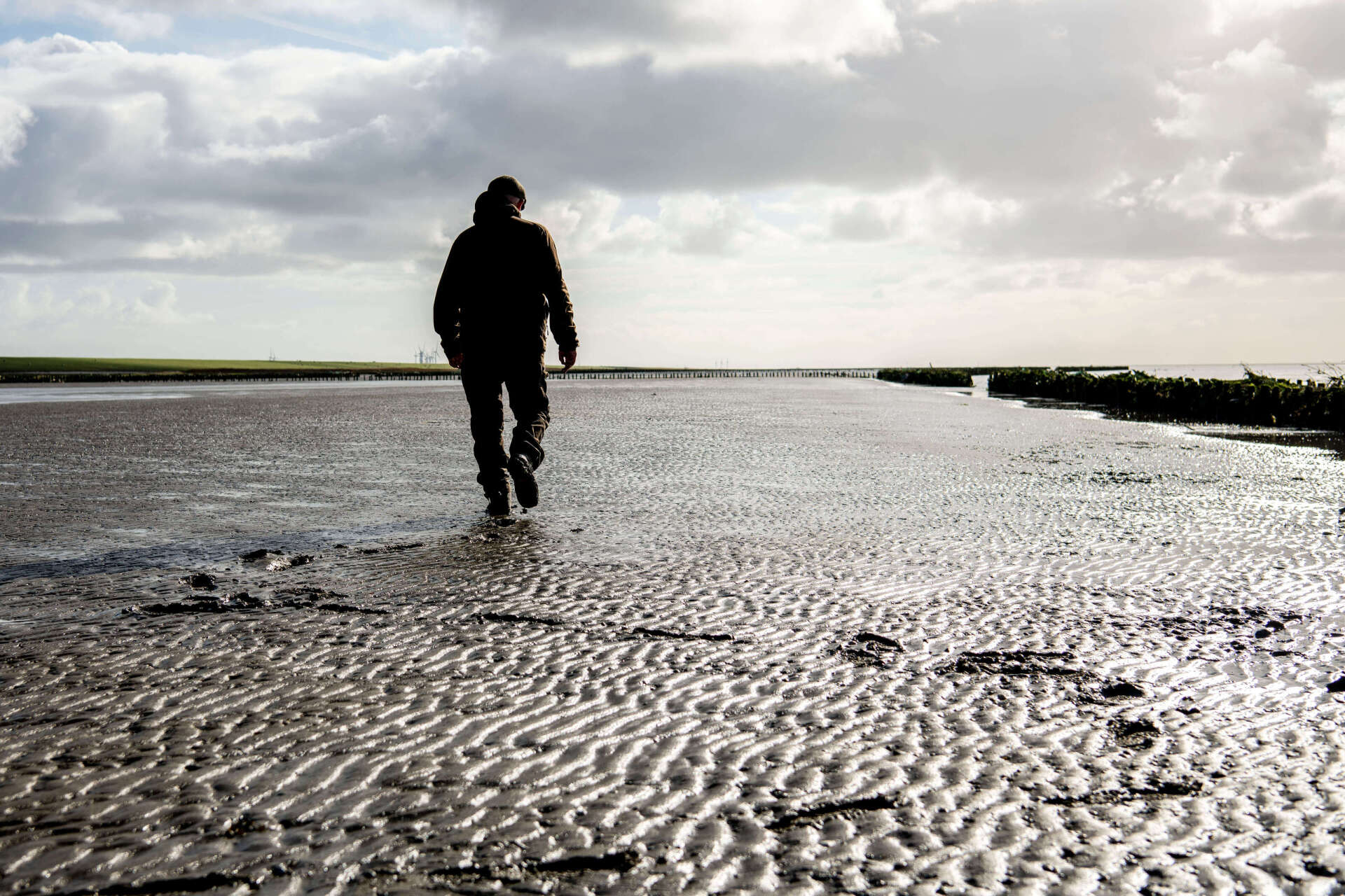En mand går over en mudret strand.