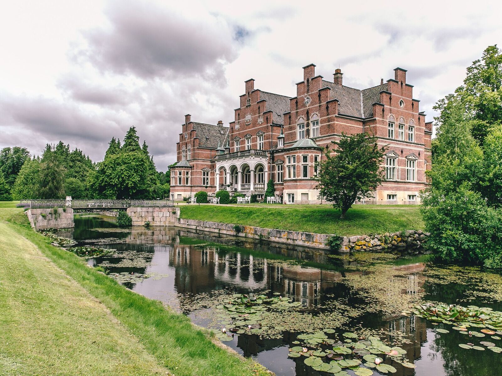 En stor murstensbygning spejler sig i vandet i en dam.