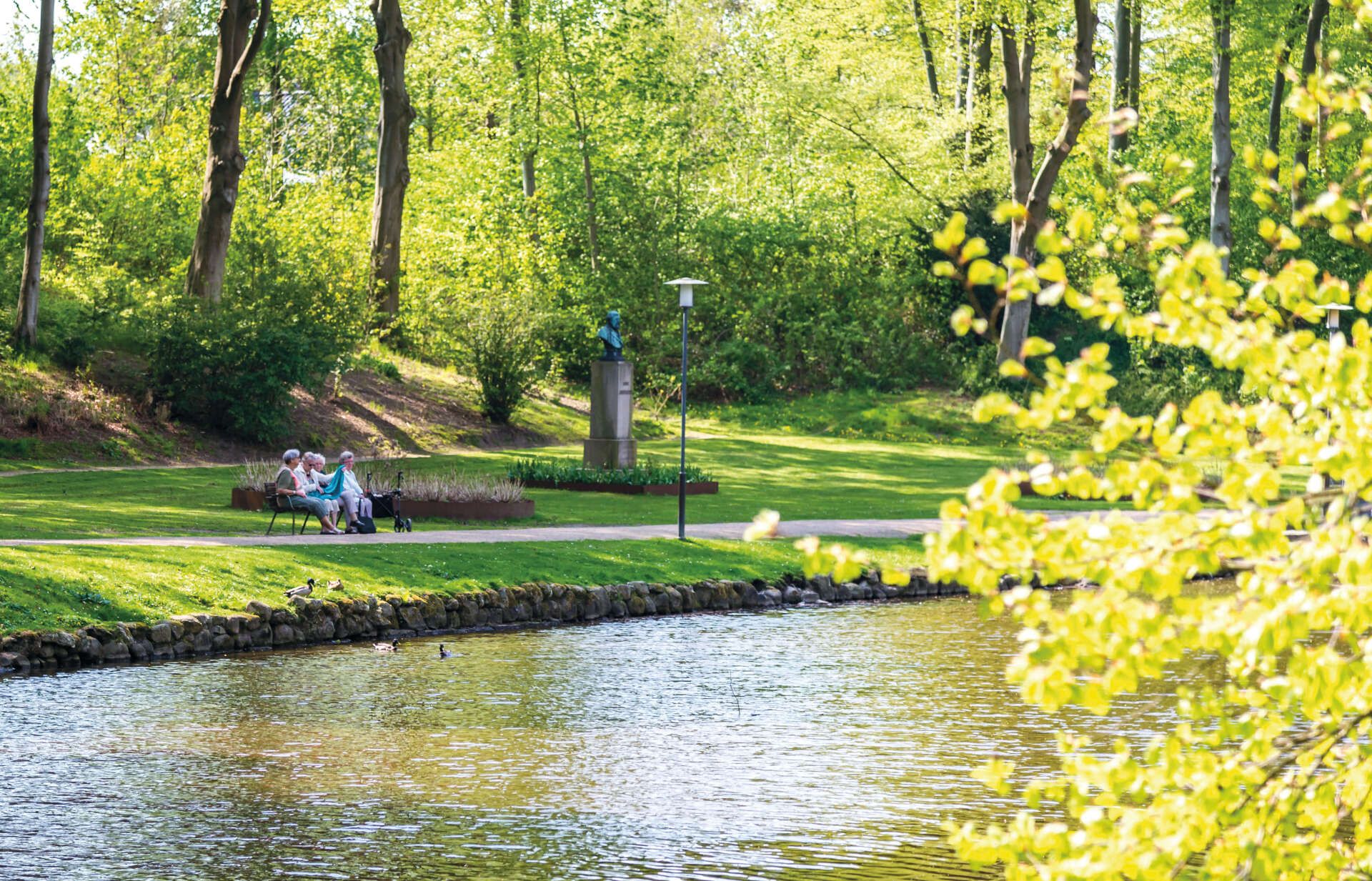 Et par sidder på en bænk ved siden af ​​en sø i en park.
