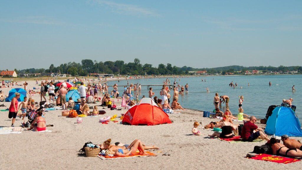 En strand fyldt med mennesker og telte på en solskinsdag.