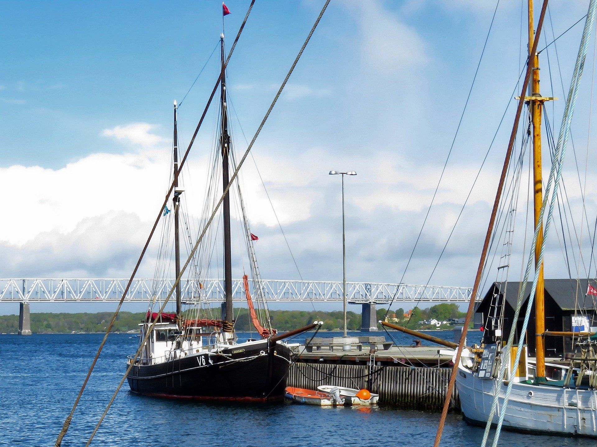 Flere både ligger til kaj i en havn med en bro i baggrunden