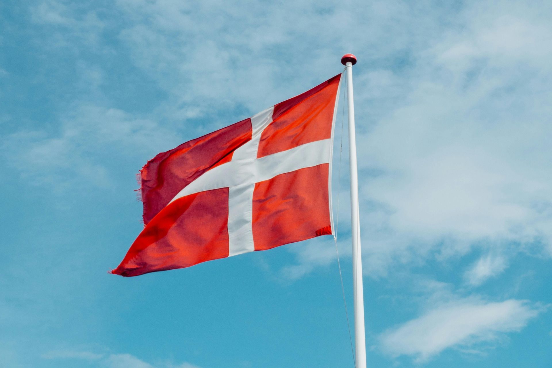 Et rødt og hvidt flag vajer i vinden mod en blå himmel.