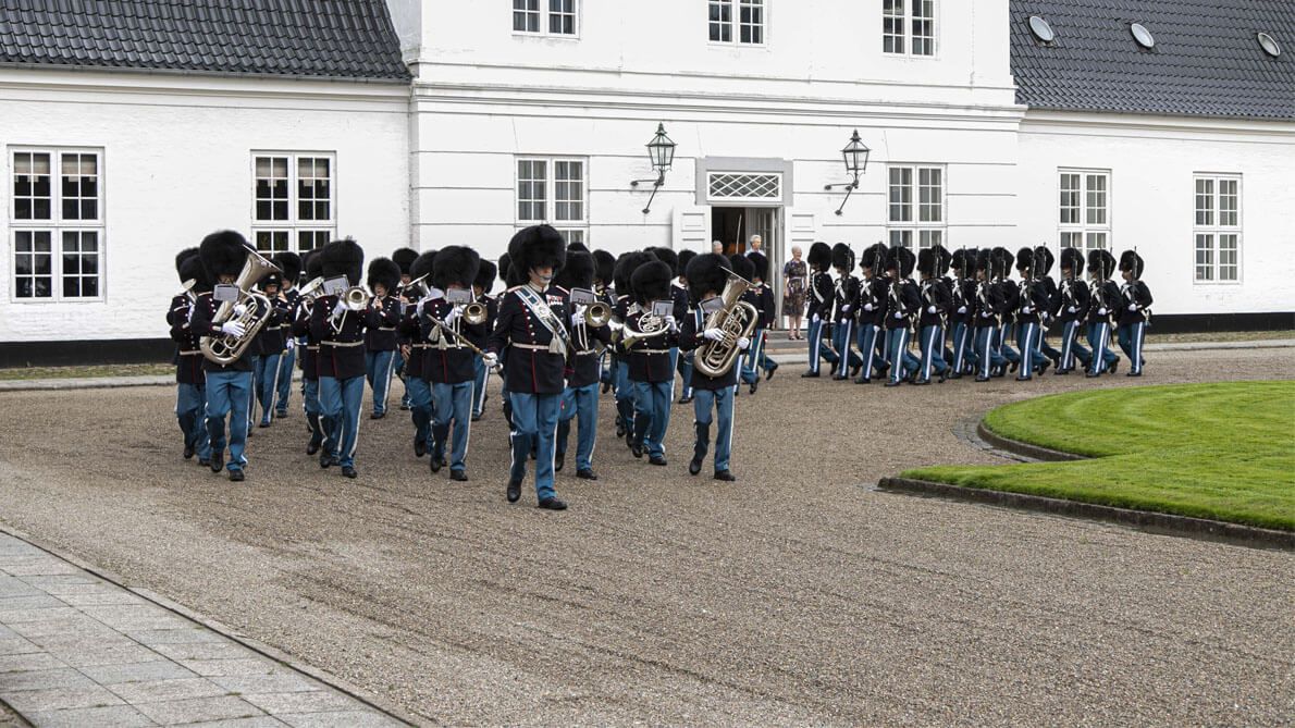 En flok soldater, der marcherer foran en hvid bygning.