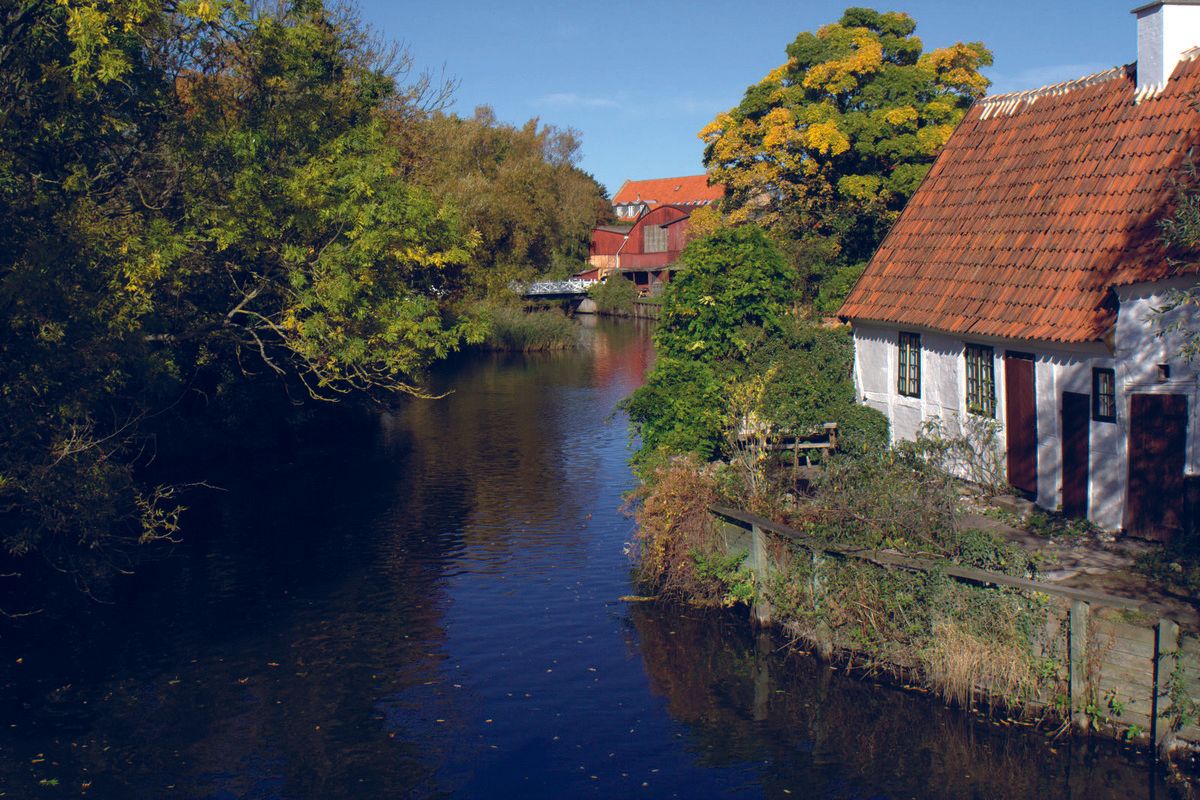 Et lille hvidt hus ligger ved siden af ​​en flod omgivet af træer.