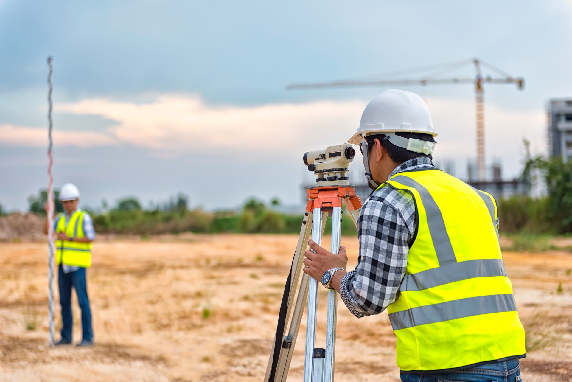 A land surveyor using a total station on a construction site with a safety vest.