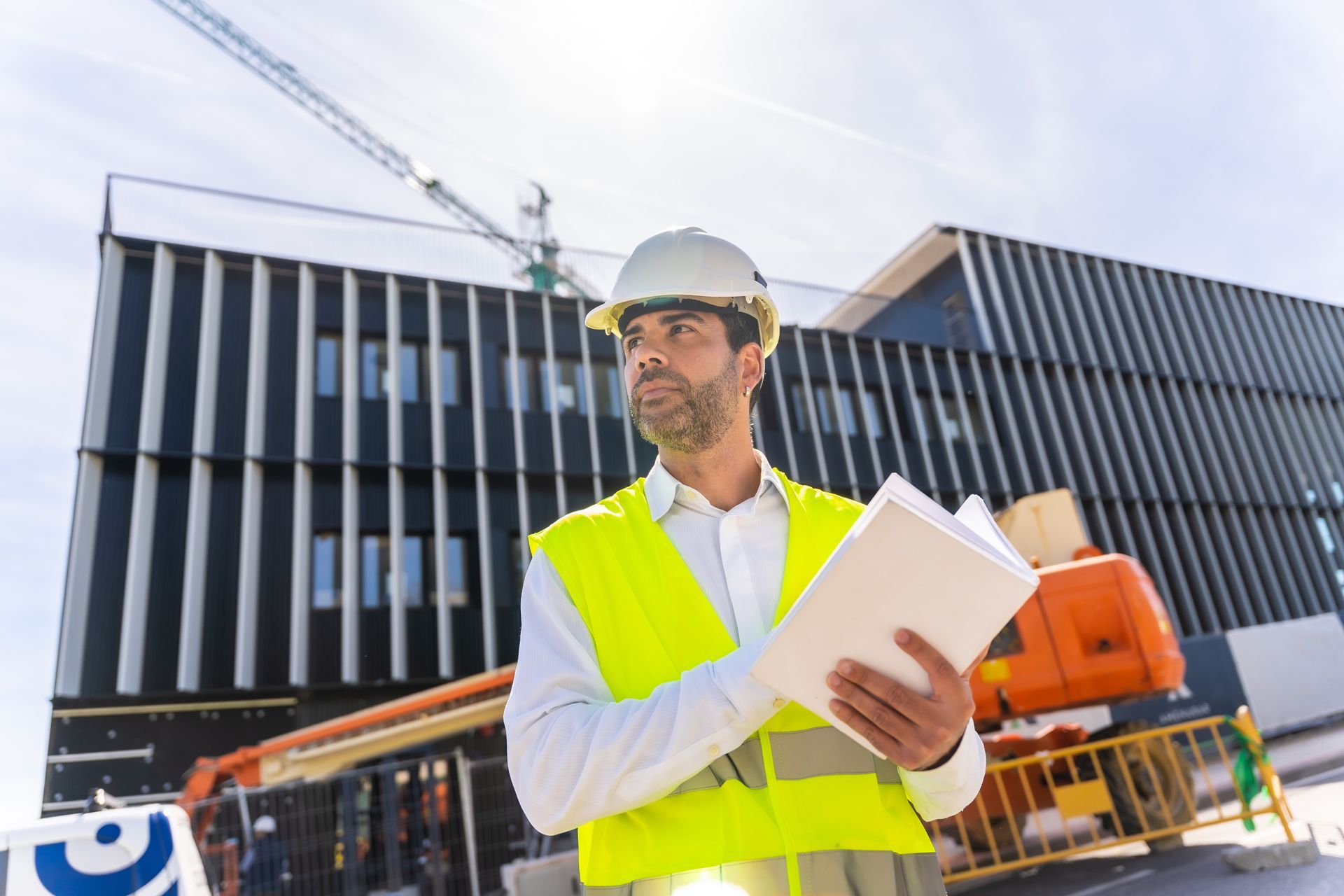 A worker with notes on his hands, next to a building under construction.