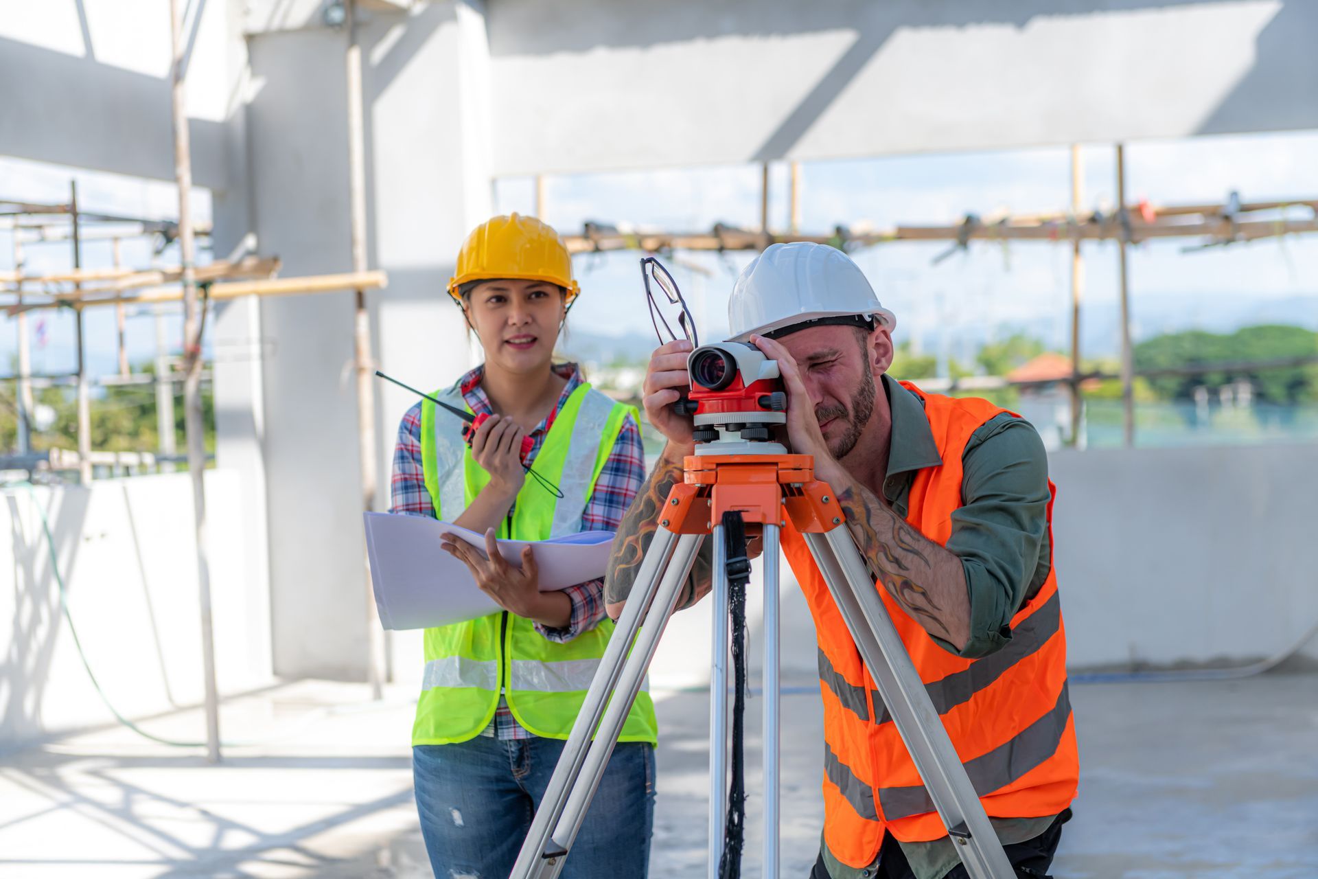 Two individuals using a surveying tool in front of Professional Land and Construction Surveyors, Aur