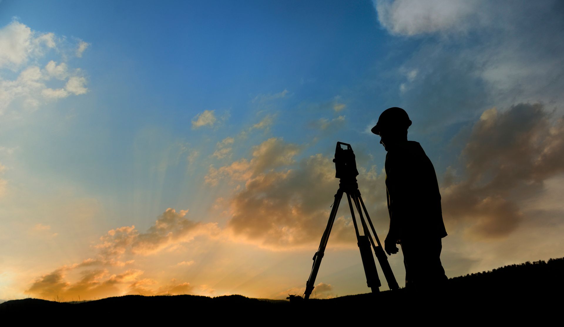 A land surveyor working with a total station, performing land surveying services, outdoors.