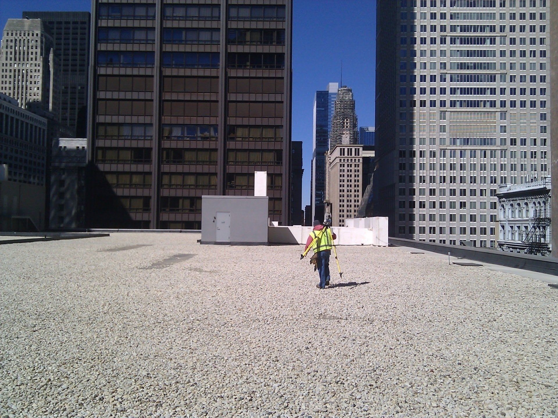 A man in a yellow vest stands on a rooftop in front of a city skyline