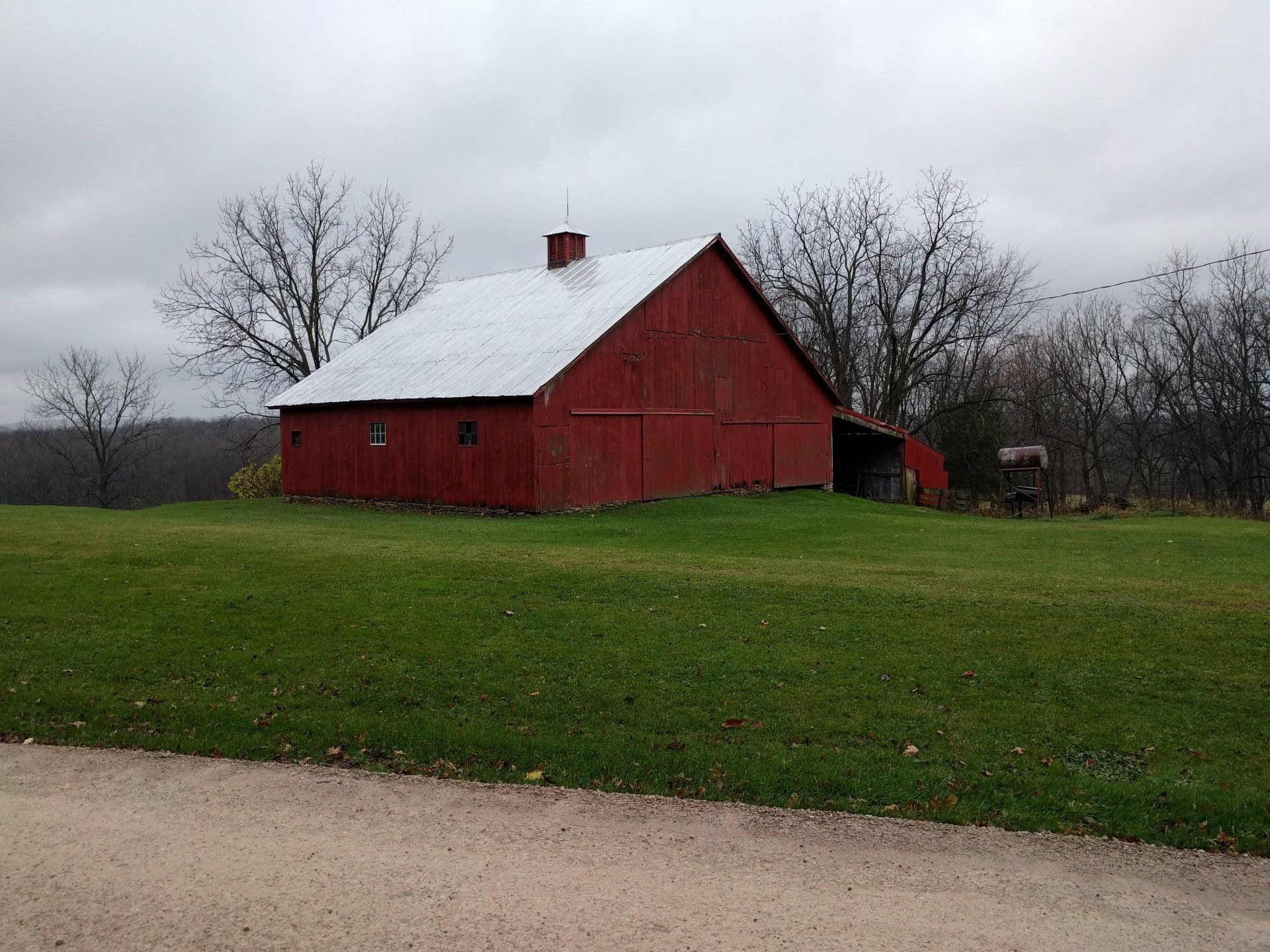 A red barn with a white roof is in the middle of a grassy field.