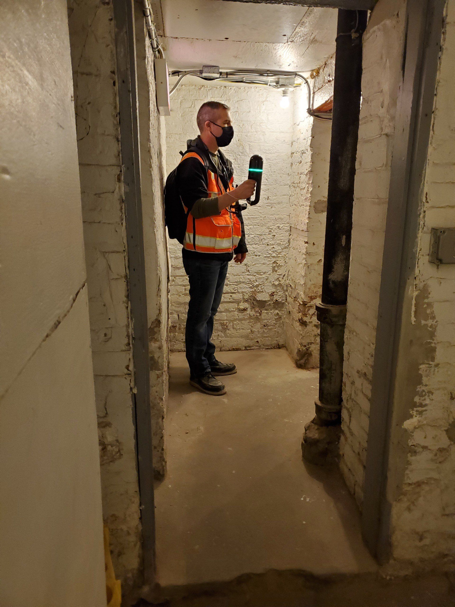 A man wearing a mask is standing in a brick room holding a microphone.