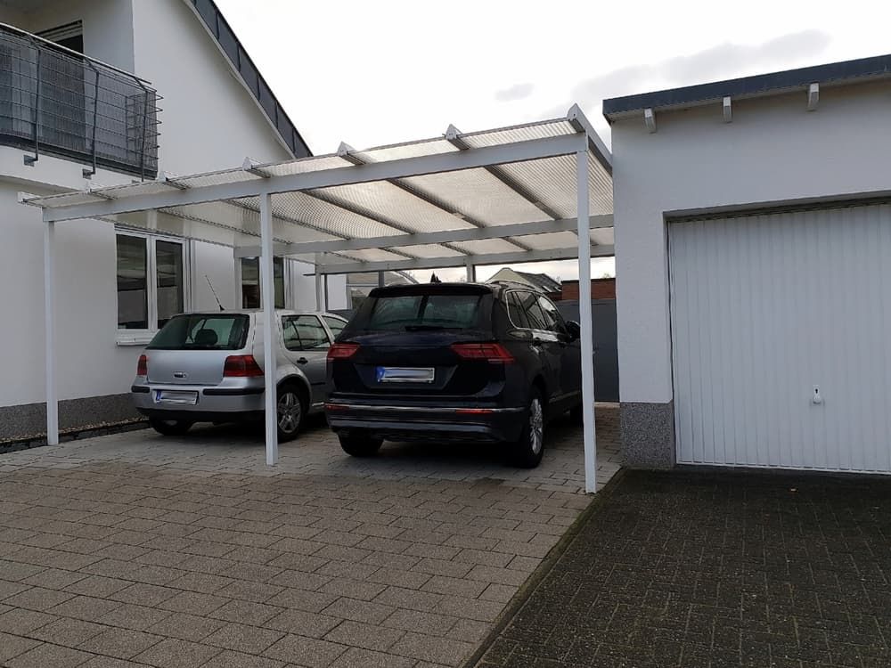 Two Cars, One Silver and One Black, Are Parked Under a White Carport Next to a Garage