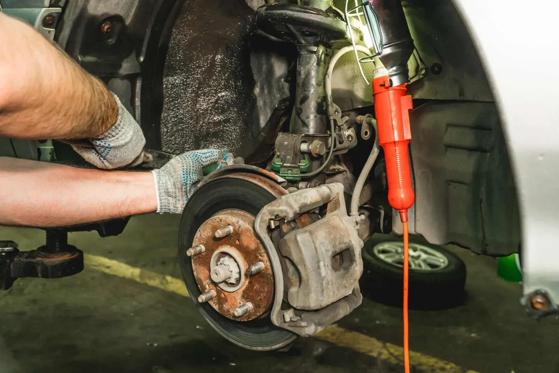 Mechanic Repairing a Car’s Brake Assembly With Tools Inside a Wheel Well — Supa Auto Services In Bundaberg, North