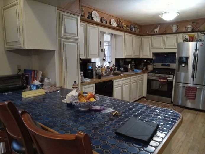 A kitchen with white cabinets, stainless steel appliances, a blue tiled countertop, and a breakfast bar.
