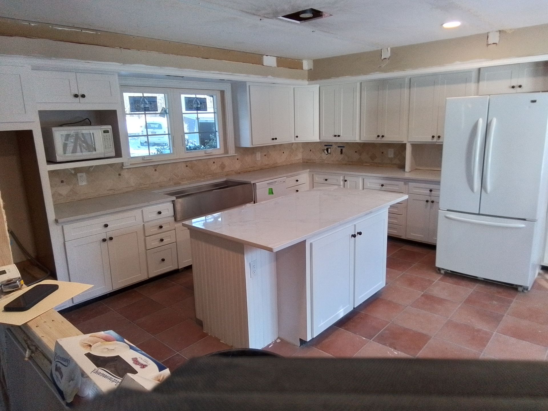 White kitchen with island, cabinets, and refrigerator, on terracotta tile floor.