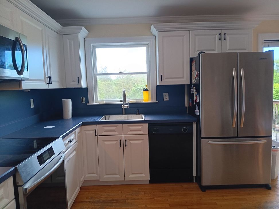 Kitchen with white cabinets, blue countertops, stainless steel appliances, and a window.