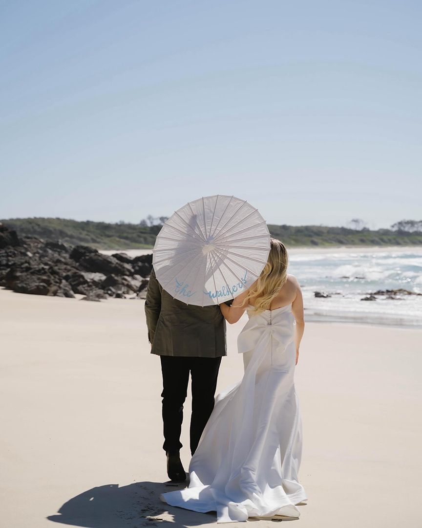 A Bride and Groom Are Standing on A Beach Holding an Umbrella — Seed + Salt Photography In Smithtown, NSW