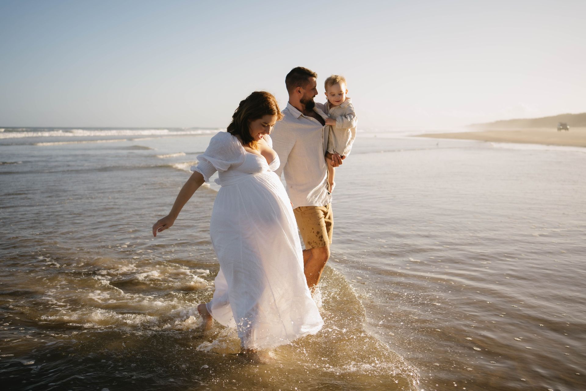 A Man Holding a Child and A Pregnant Woman Are Splashing in the Ocean — Seed + Salt Photography In Smithtown, NSW