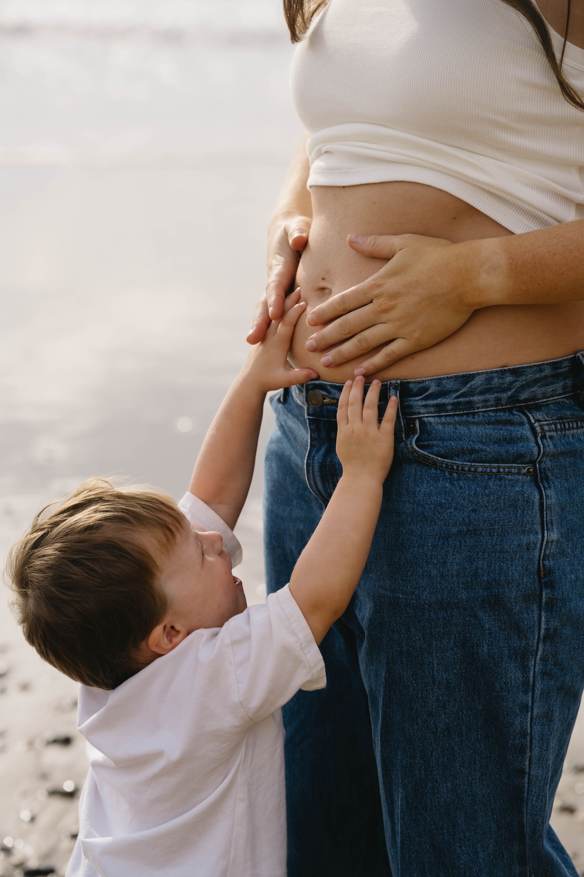 Todler reaching up to touch his pregnant mothers stomach