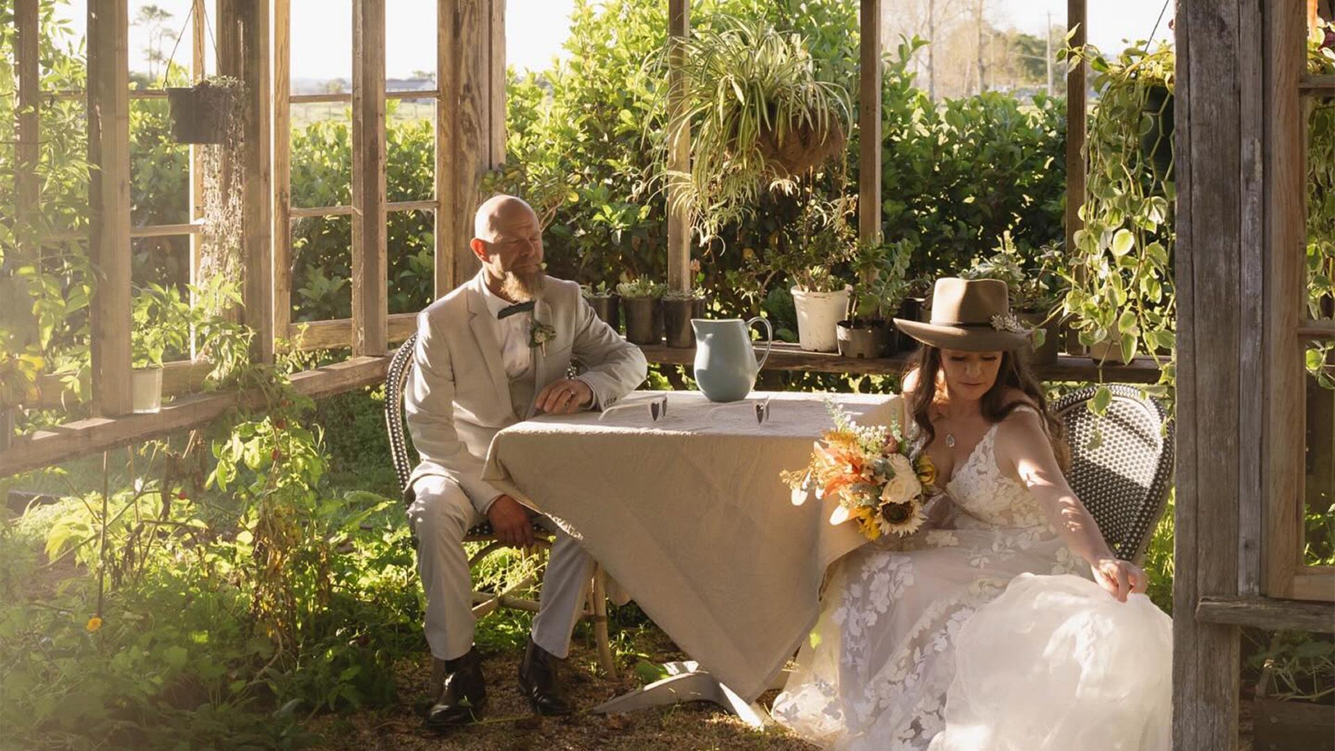 A Bride and Groom Are Sitting at A Table in A Greenhouse — Seed + Salt Photography In Smithtown, NSW