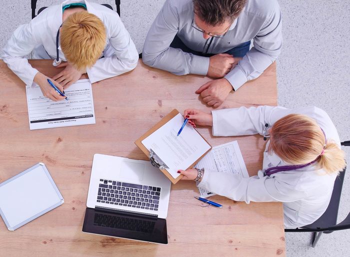 A group of doctors are sitting at a table with papers and a laptop.