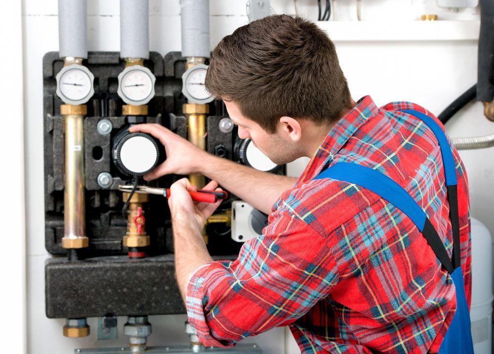 A Man in A Plaid Shirt and Blue Overalls Is Working on A Machine — Gillespie Plumbing in Grafton, NSW