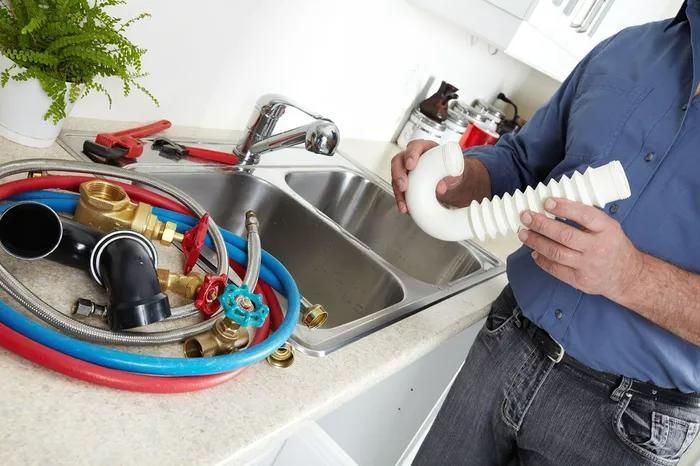 A Man Is Holding a Pipe in Front of A Sink — Gillespie Plumbing in Grafton, NSW