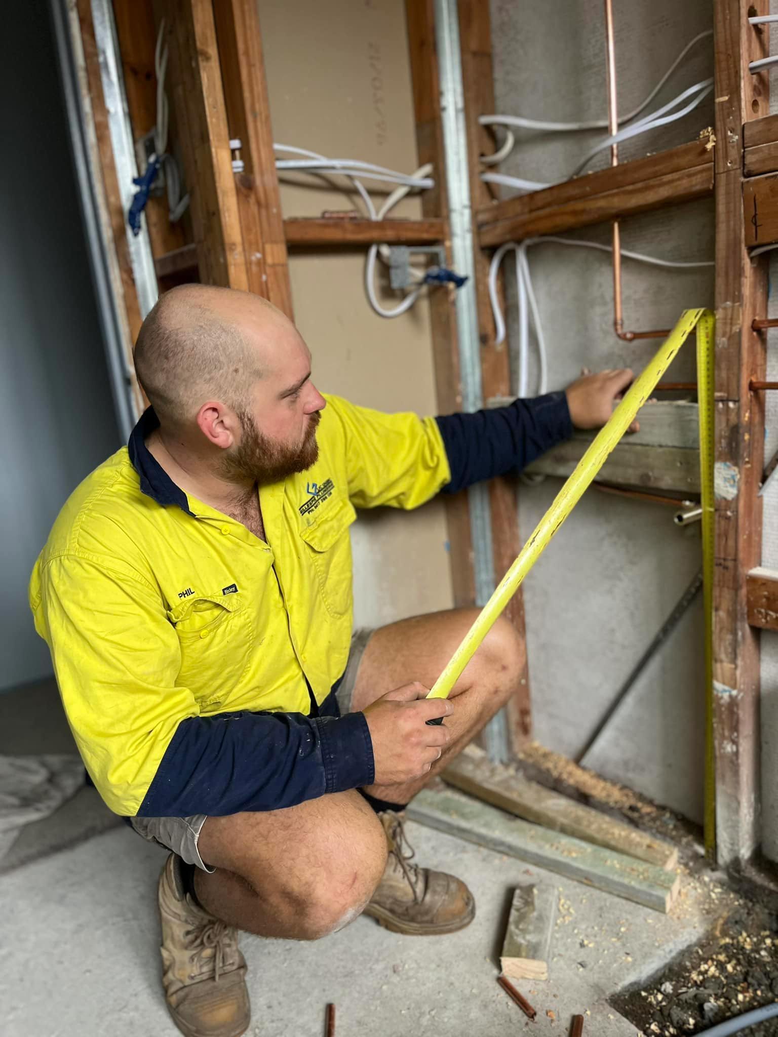A Man Is Measuring a Pipe with A Tape Measure — Gillespie Plumbing in Grafton, NSW