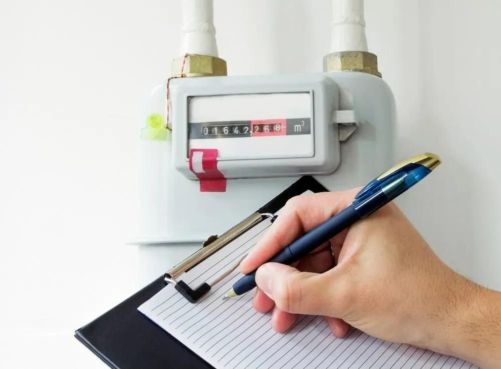 A Person Is Writing on A Clipboard in Front of A Gas Meter — Gillespie Plumbing in Grafton, NSW