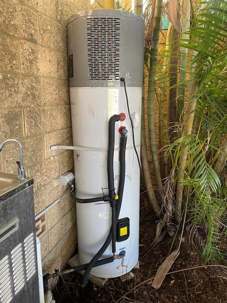 A White Water Heater Is Sitting Next to A Brick Wall — Gillespie Plumbing in Grafton, NSW
