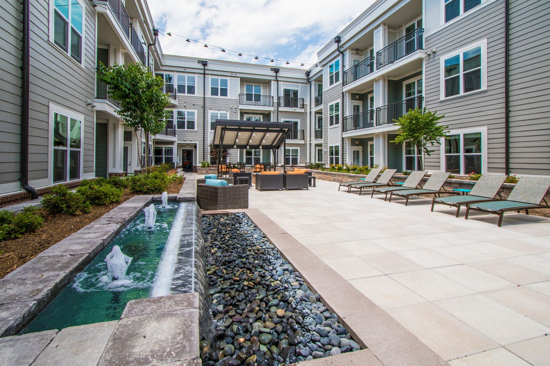 Courtyard with a fountain, seating area, and multi-story apartment buildings.