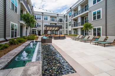 Courtyard with a fountain, seating area, and multi-story apartment buildings.