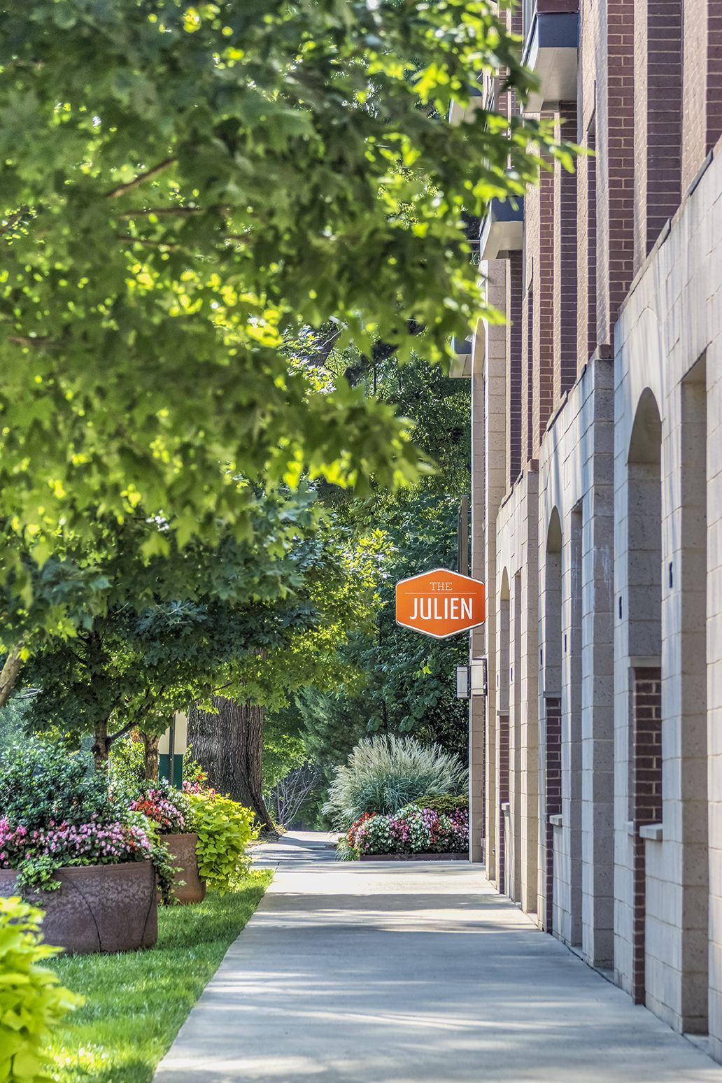 Sidewalk with lush greenery, stone building, orange 