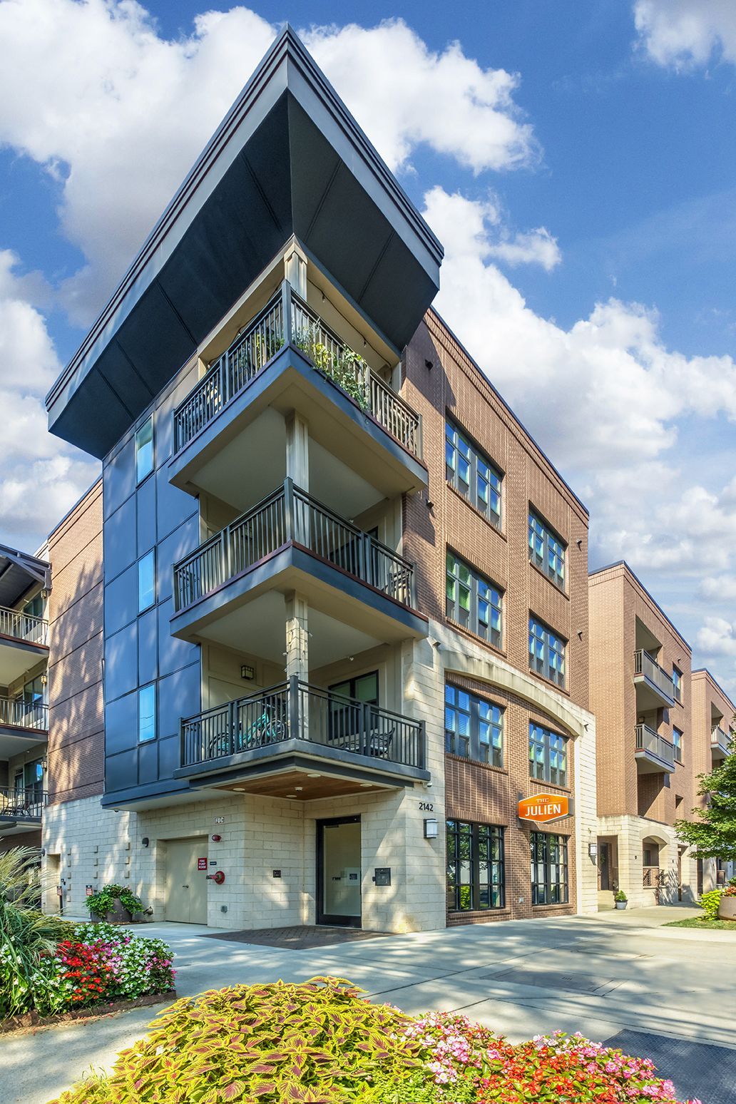 Multi-story brick and blue-paneled building with balconies, under a blue sky with clouds.