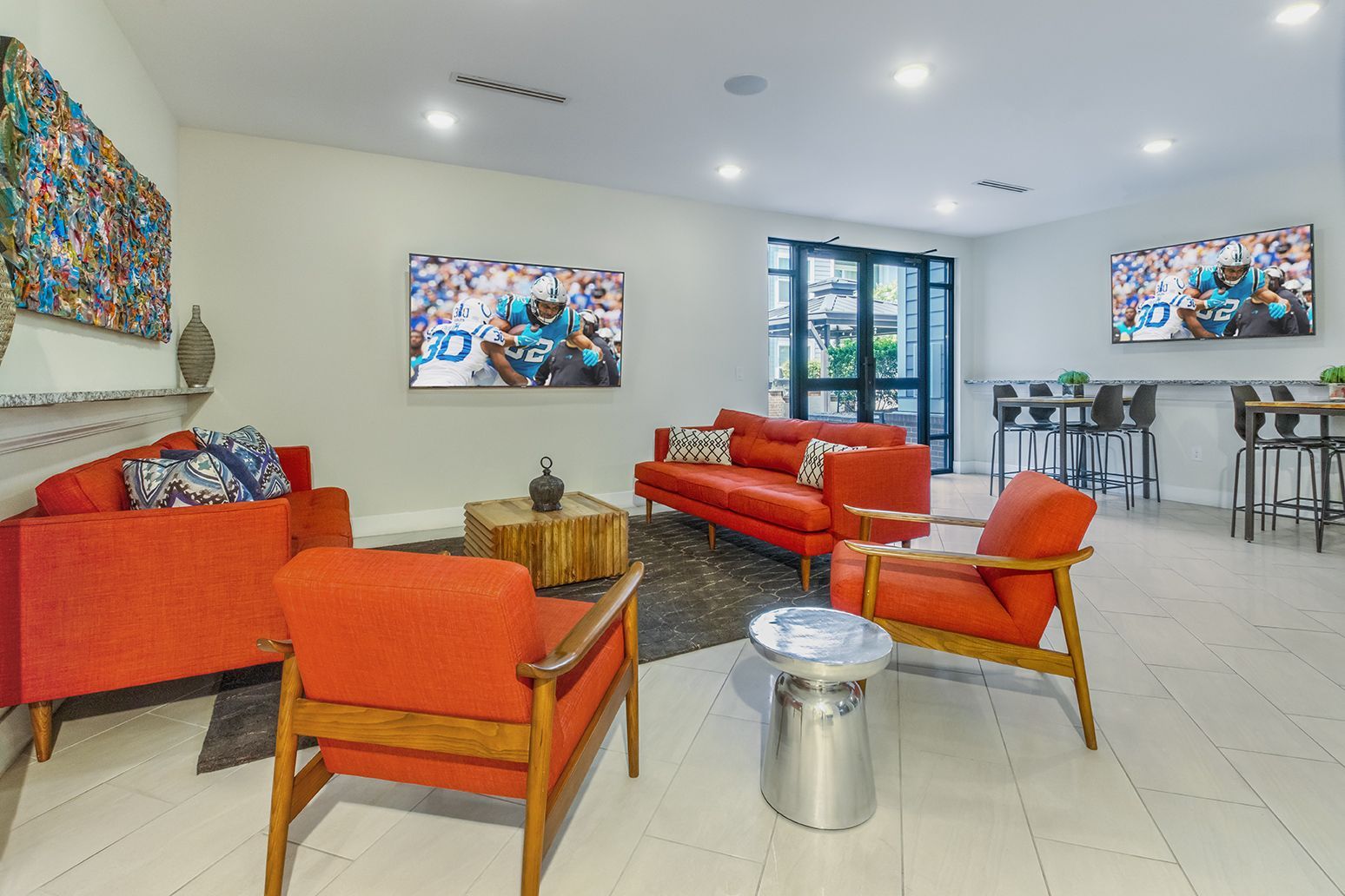 Lounge area with orange sofas and chairs, art, high tables, and a modern door to a patio.