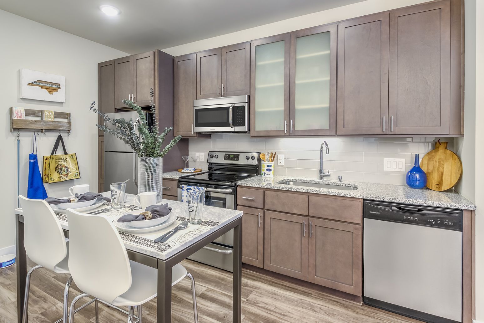 Modern kitchen with stainless steel appliances, brown cabinets, and a dining table with two white chairs.