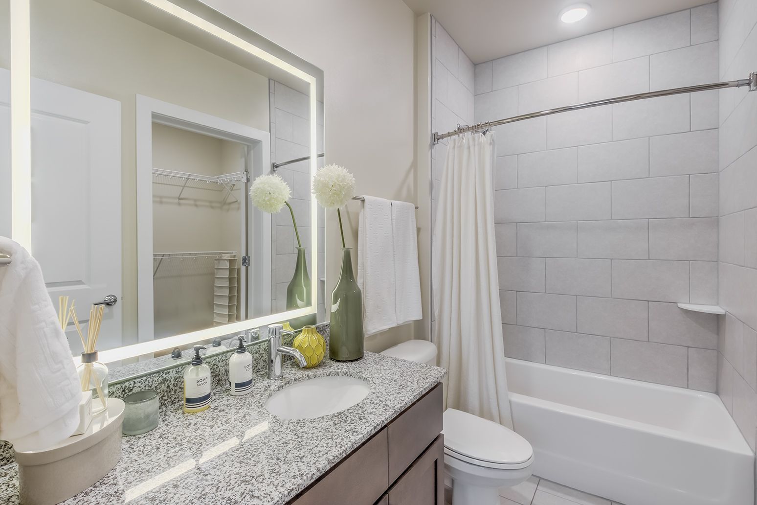 Modern bathroom with marble vanity, lit mirror, white tub, and tiled shower.