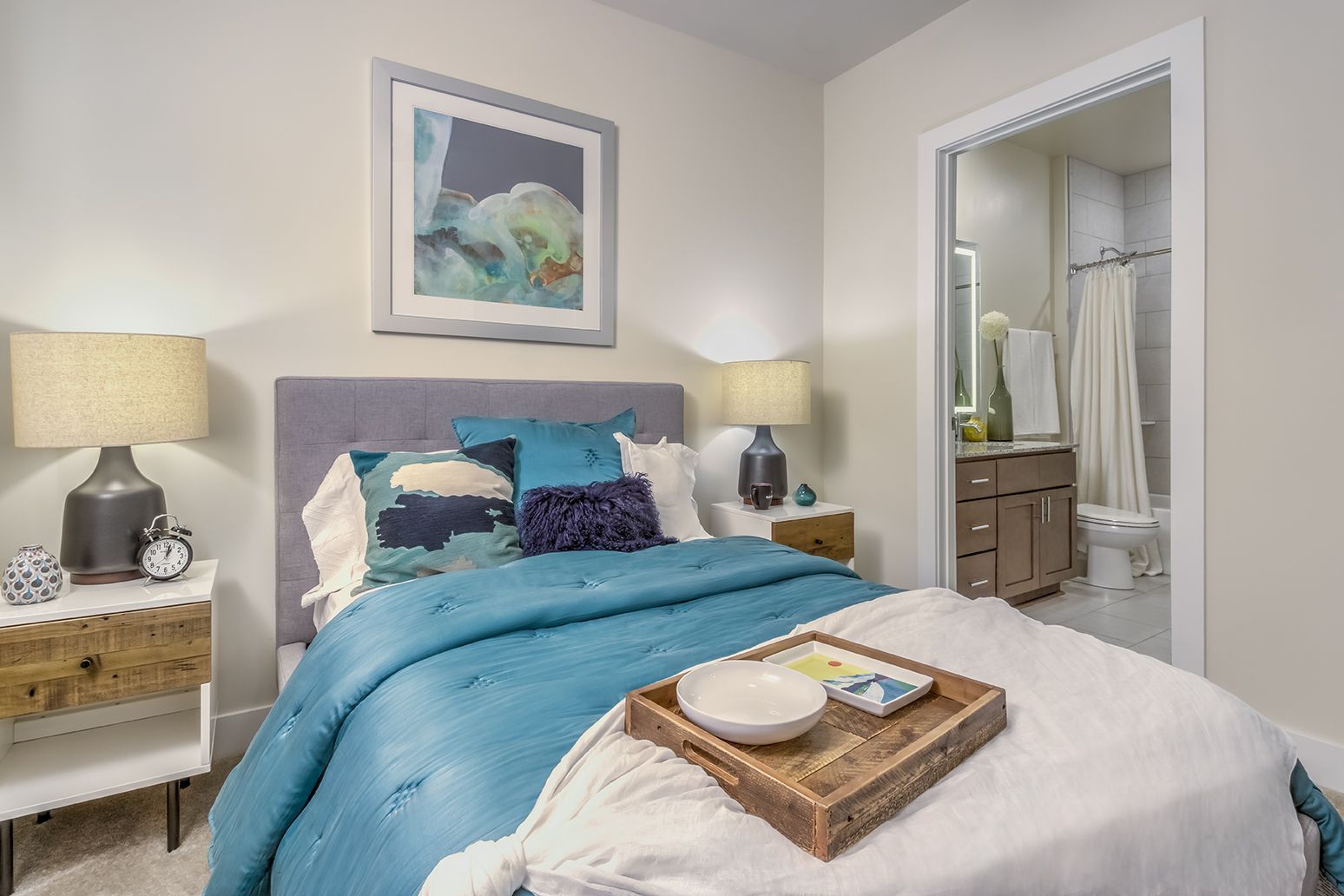 Bedroom with a bed, nightstands, lamps, and a view into a bathroom. Teal and blue bedding.