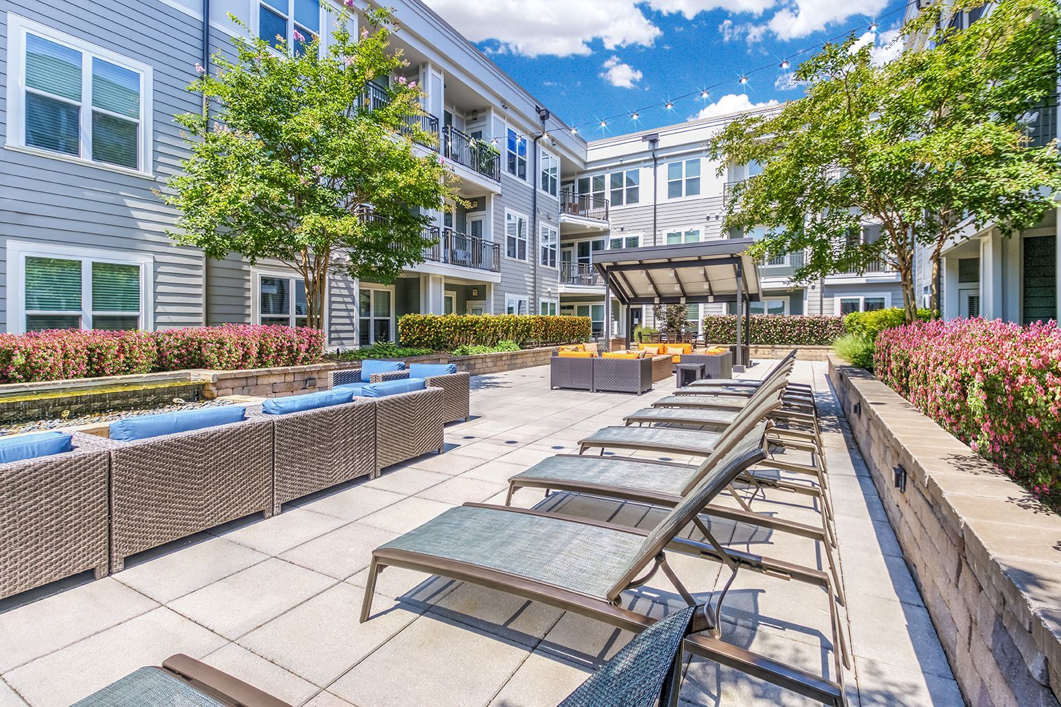 Outdoor patio with lounge chairs, sofas, and a pergola. Apartments in the background.