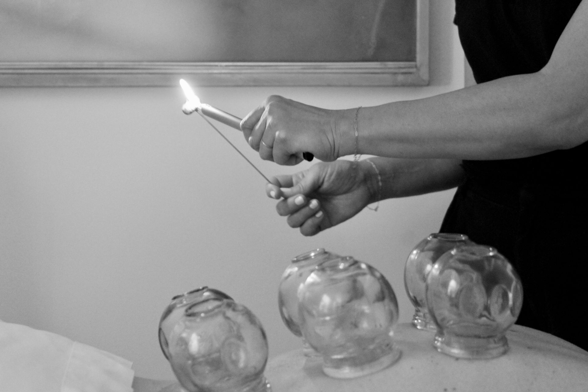 Hands holding a lit match near glass jars on a table, creating a flame.