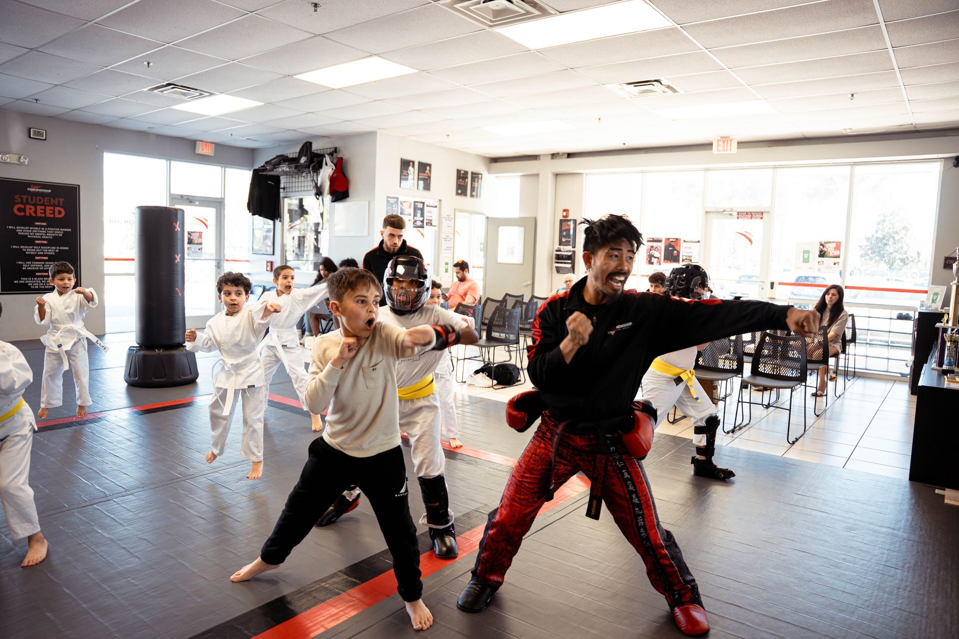 People in white martial arts uniforms sitting on a mat, being addressed by an instructor.