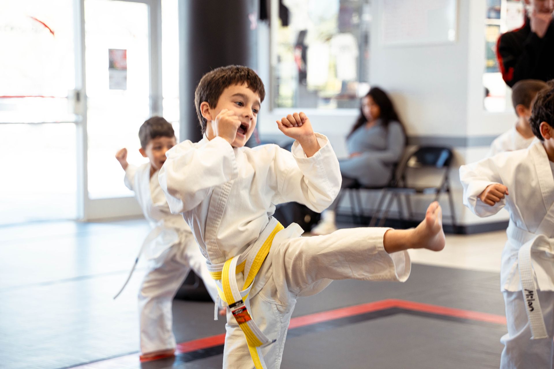 Two people in taekwondo gear sparring in a gym, one kicking towards the other.