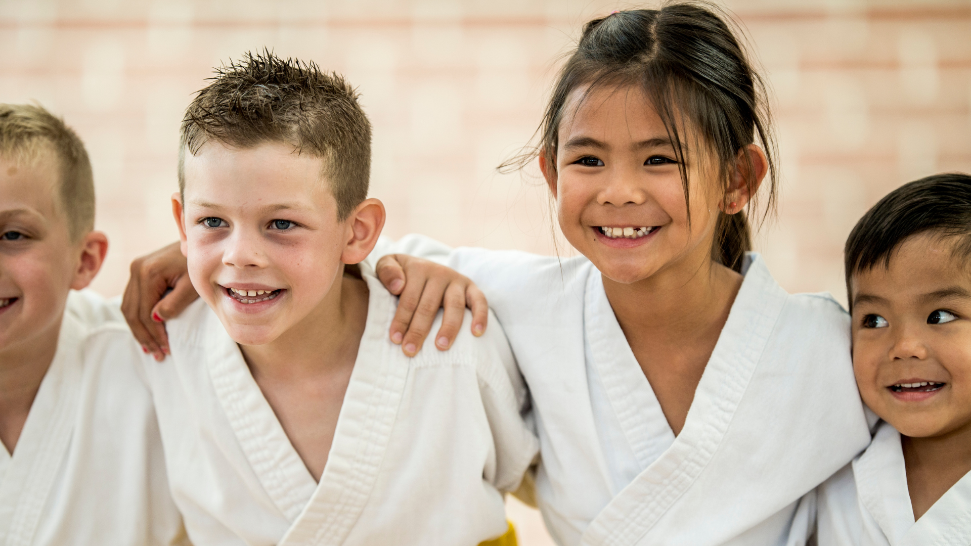 Four children in karate uniforms smiling, arms around each other.