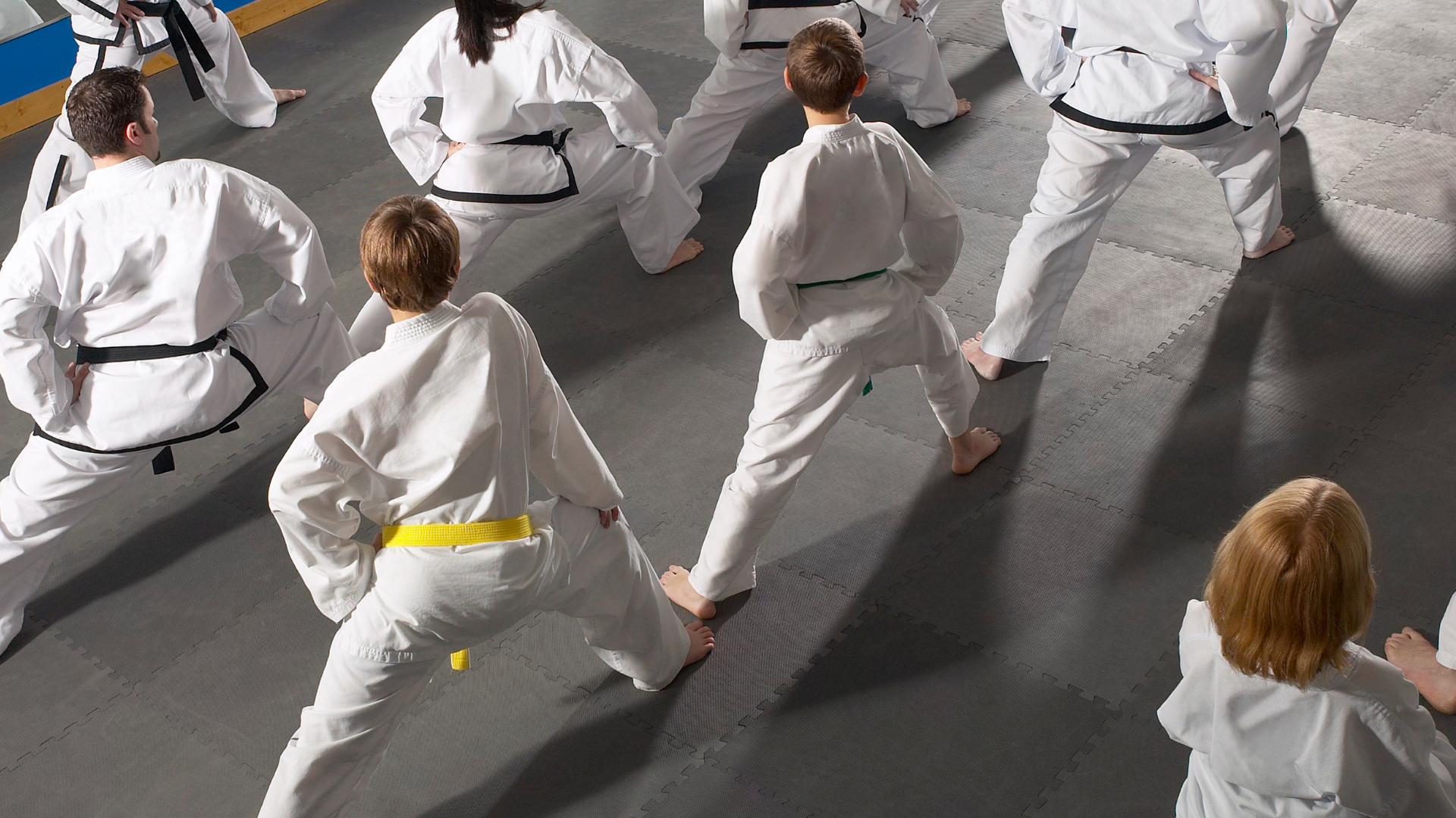 People in white martial arts uniforms stretching in a training room.