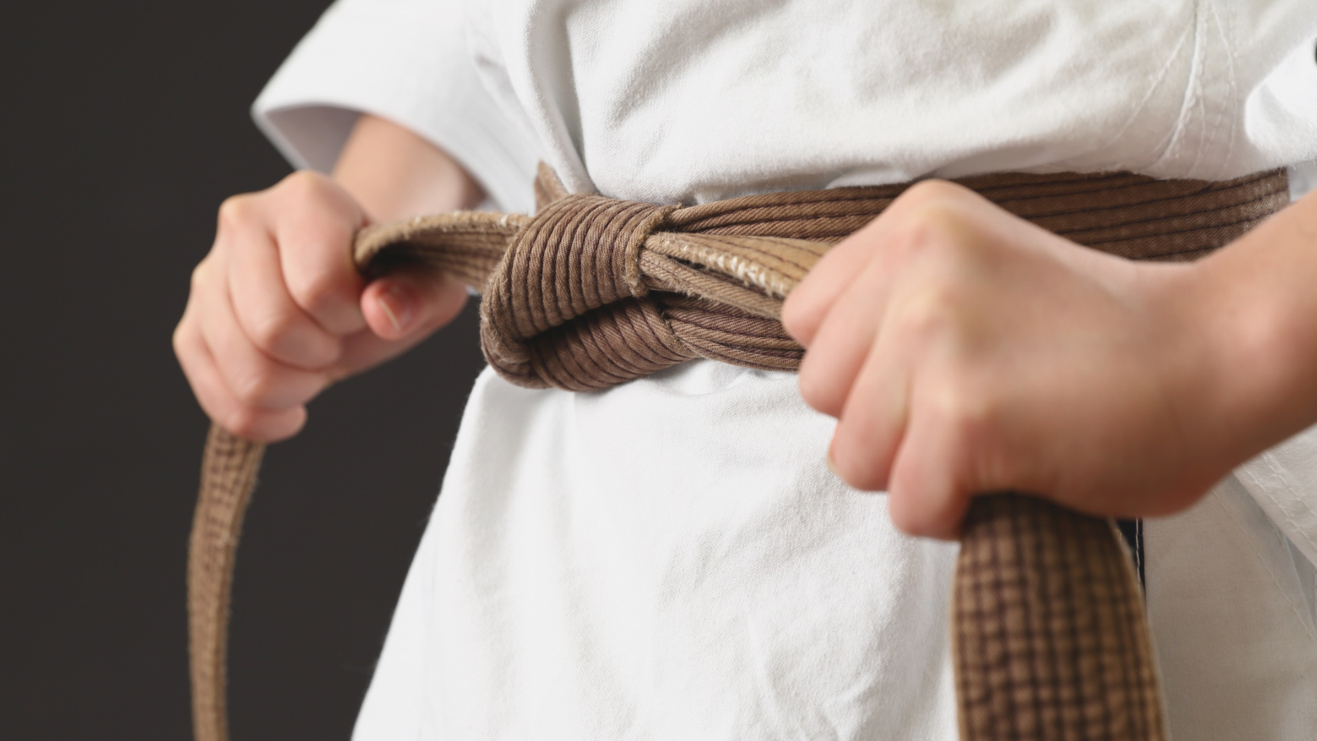 Person tying a brown karate belt around a white gi.