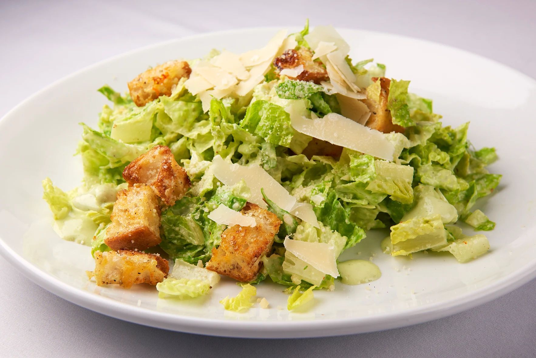 A close up of a salad on a white plate on a table.