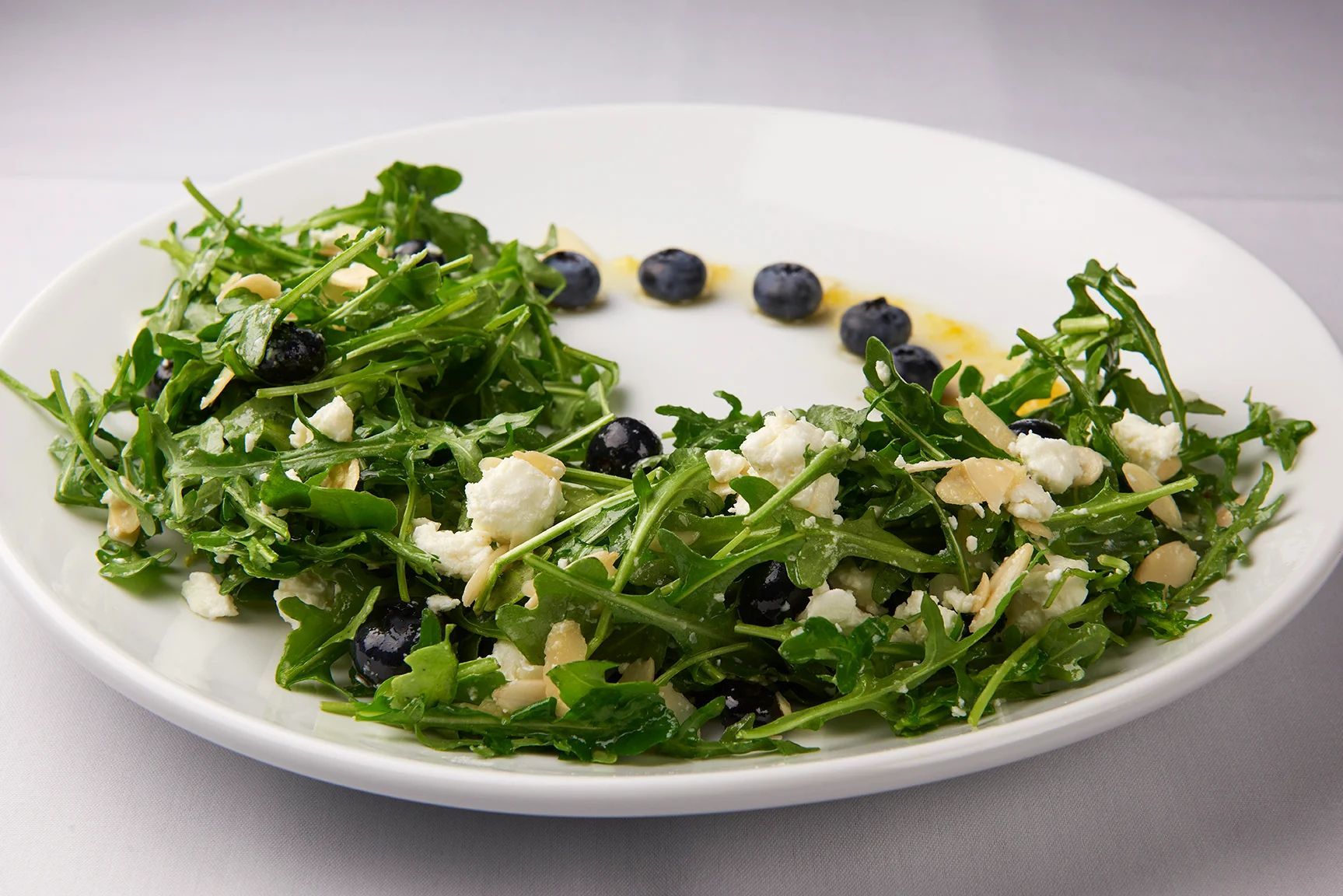 A white plate topped with a salad with blueberries and cheese.