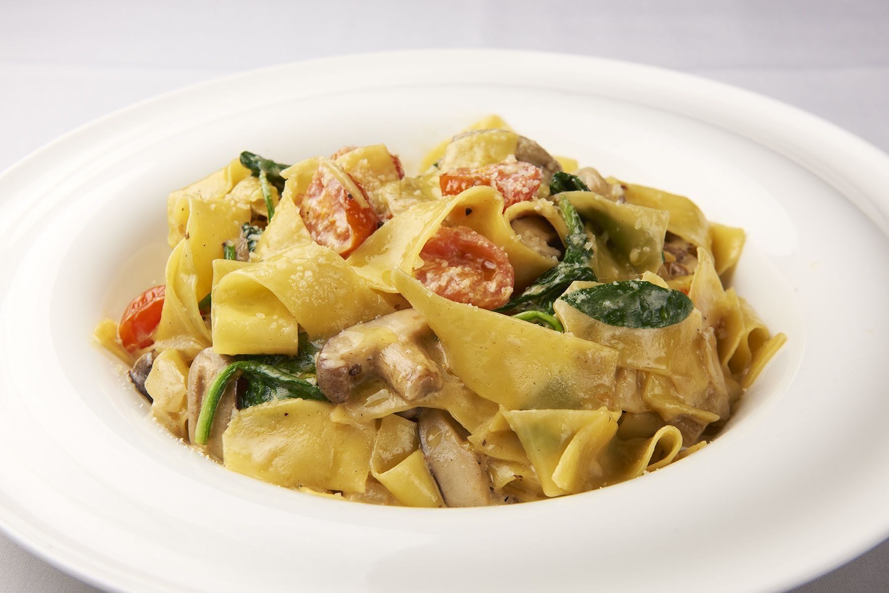 A white plate topped with pasta tomatoes and spinach