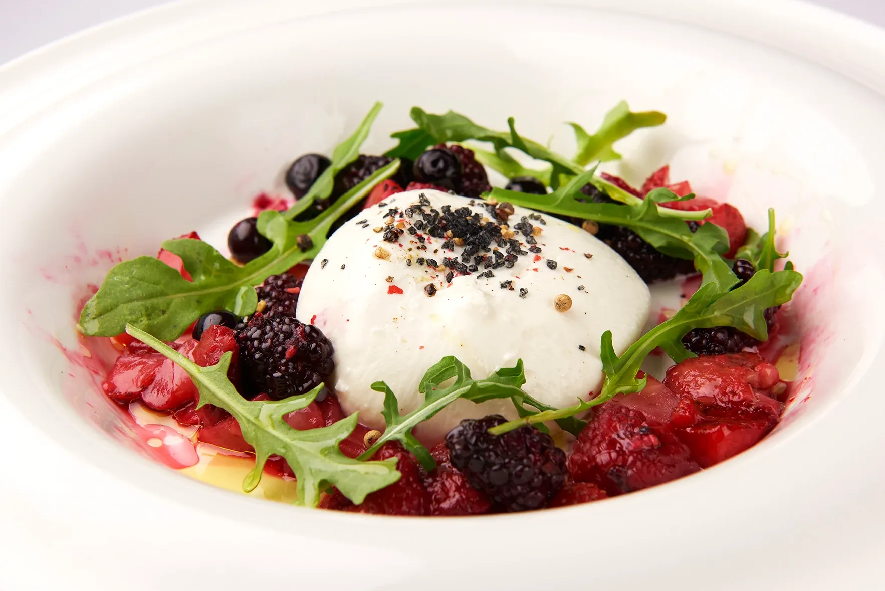 A white plate topped with a salad of berries and yogurt.